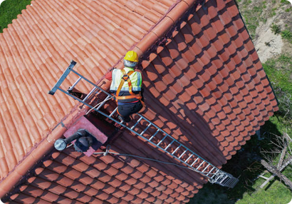 Roofing professional working on red tile roof with safety equipment